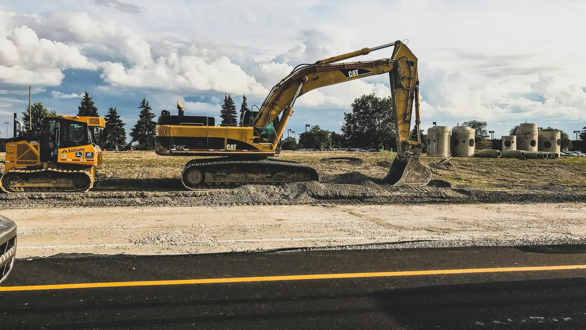 Excavator working on a new highway alignment beside freshly laid asphalt
